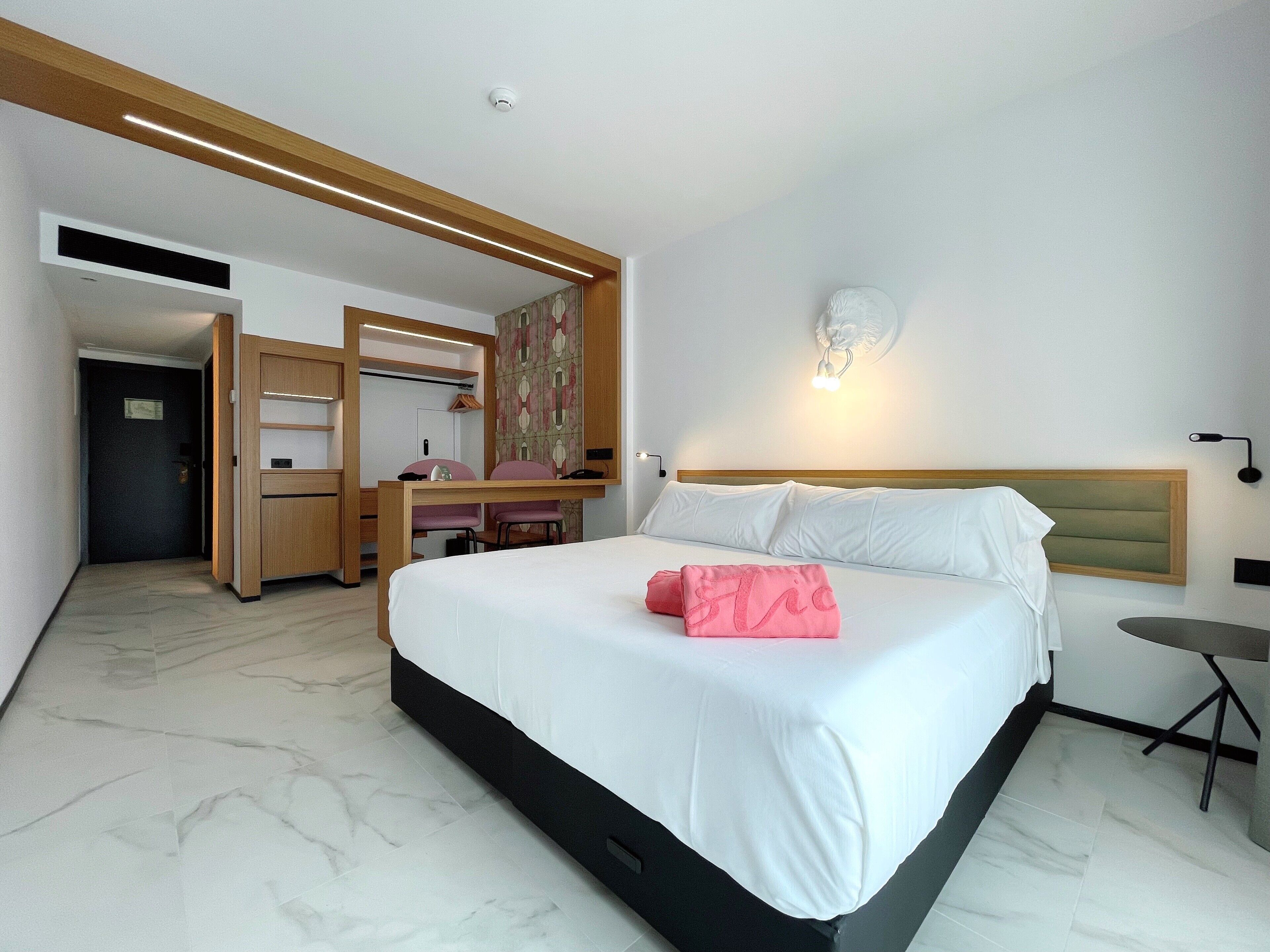 A hotel room with a bed, a desk, a chair, and a small table.