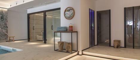 A modern interior with a pool, a wooden stool, a table with a vase, and a large mirror.