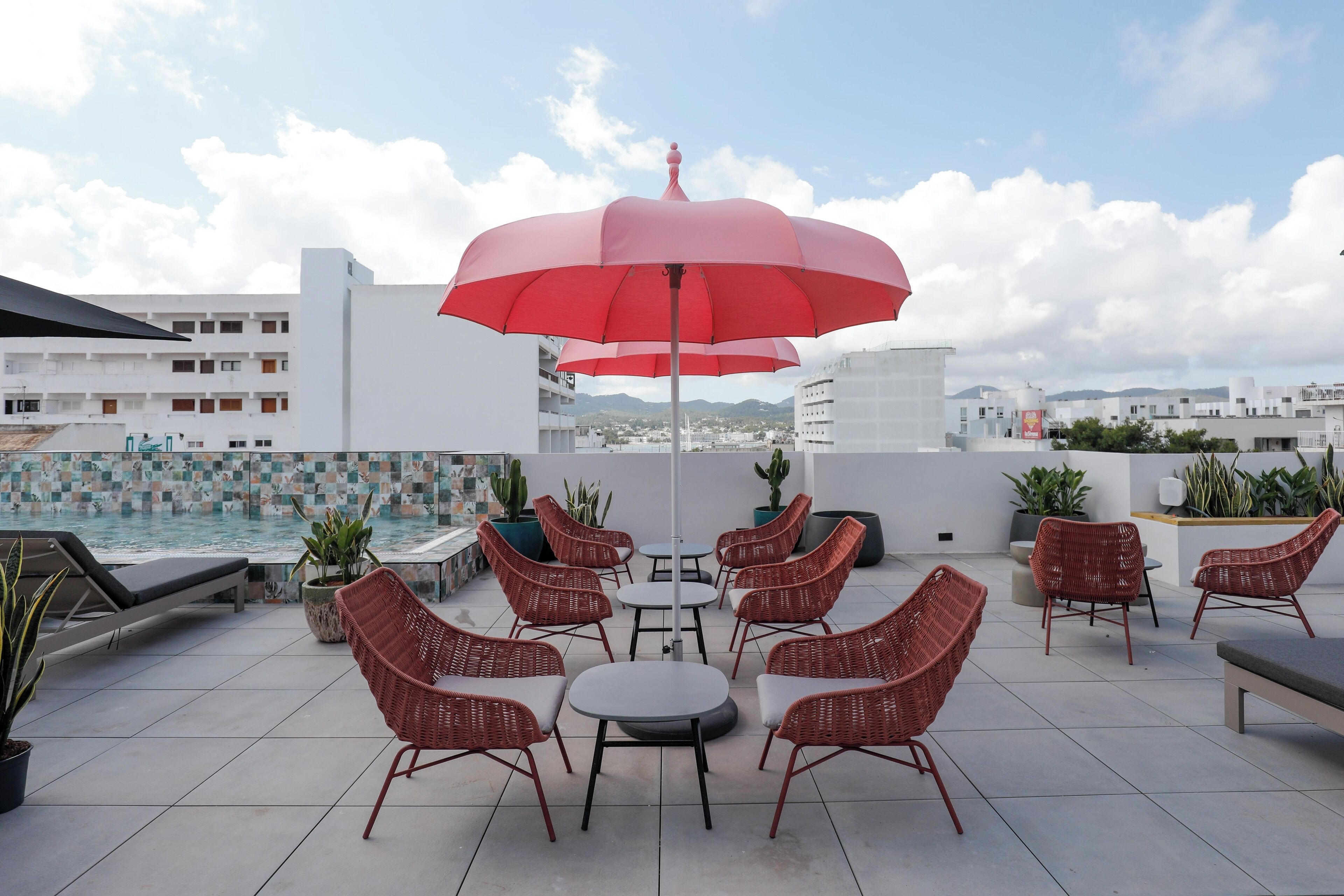 Terraza en la azotea con sillas de mimbre, una mesa y un paraguas rojo.
