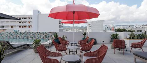 Terraza en la azotea con sillas de mimbre, una mesa y un paraguas rojo.