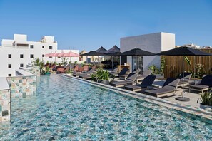 Un espace piscine aménagé sur le toit, avec des chaises longues et des parasols, entouré d’immeubles.