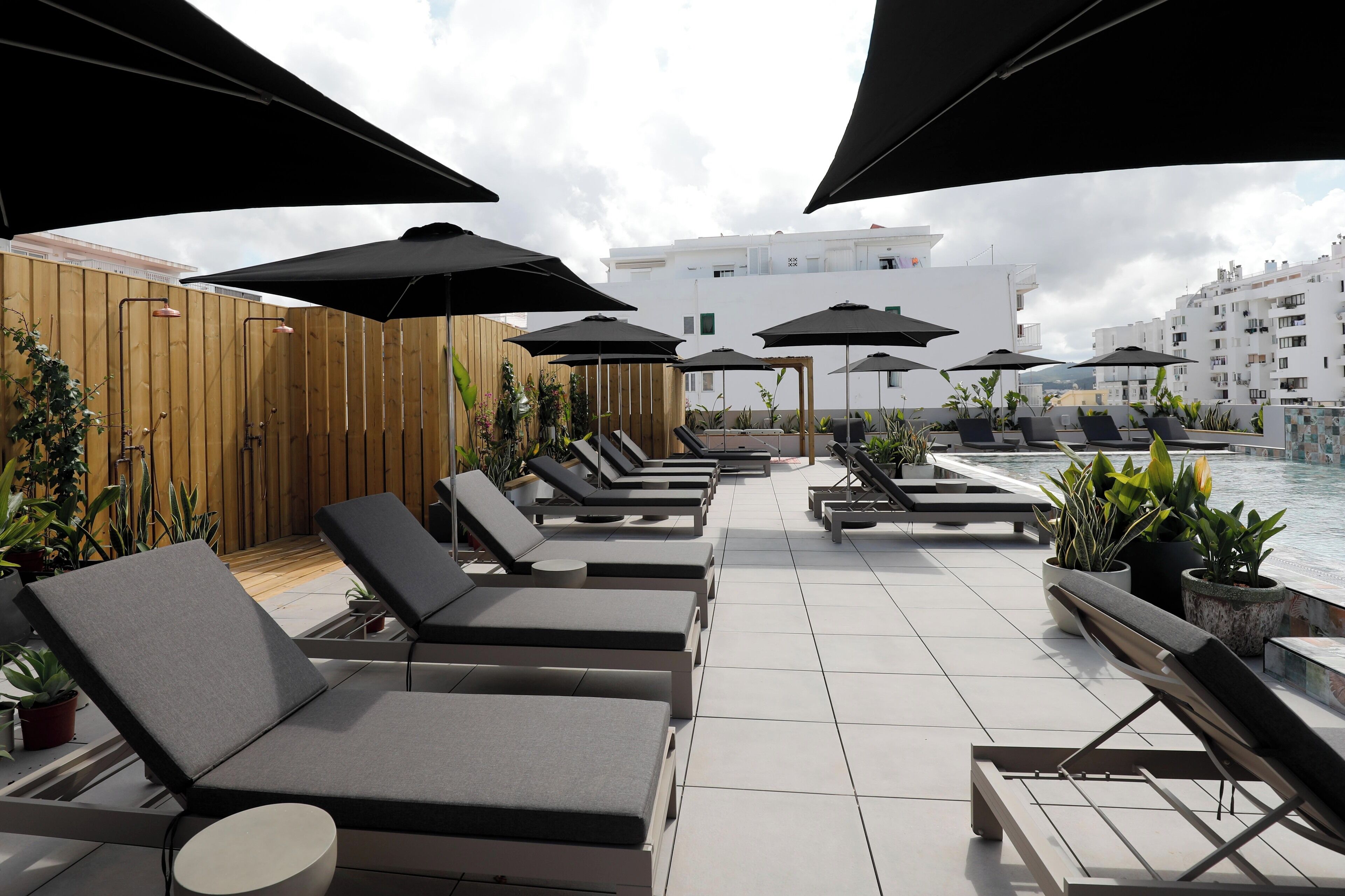 A rooftop lounge area with sun loungers, umbrellas, and potted plants.