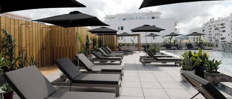 A rooftop lounge area with sun loungers, umbrellas, and potted plants.