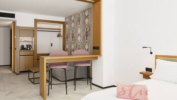 Habitación compacta con cama, escritorio con dos sillas, kitchenette y pared con diseño.