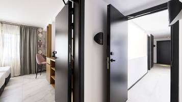 Une chambre d’hôtel moderne, équipée d’un lit, d’un bureau et d’une chaise. Une porte donne accès à une autre pièce.