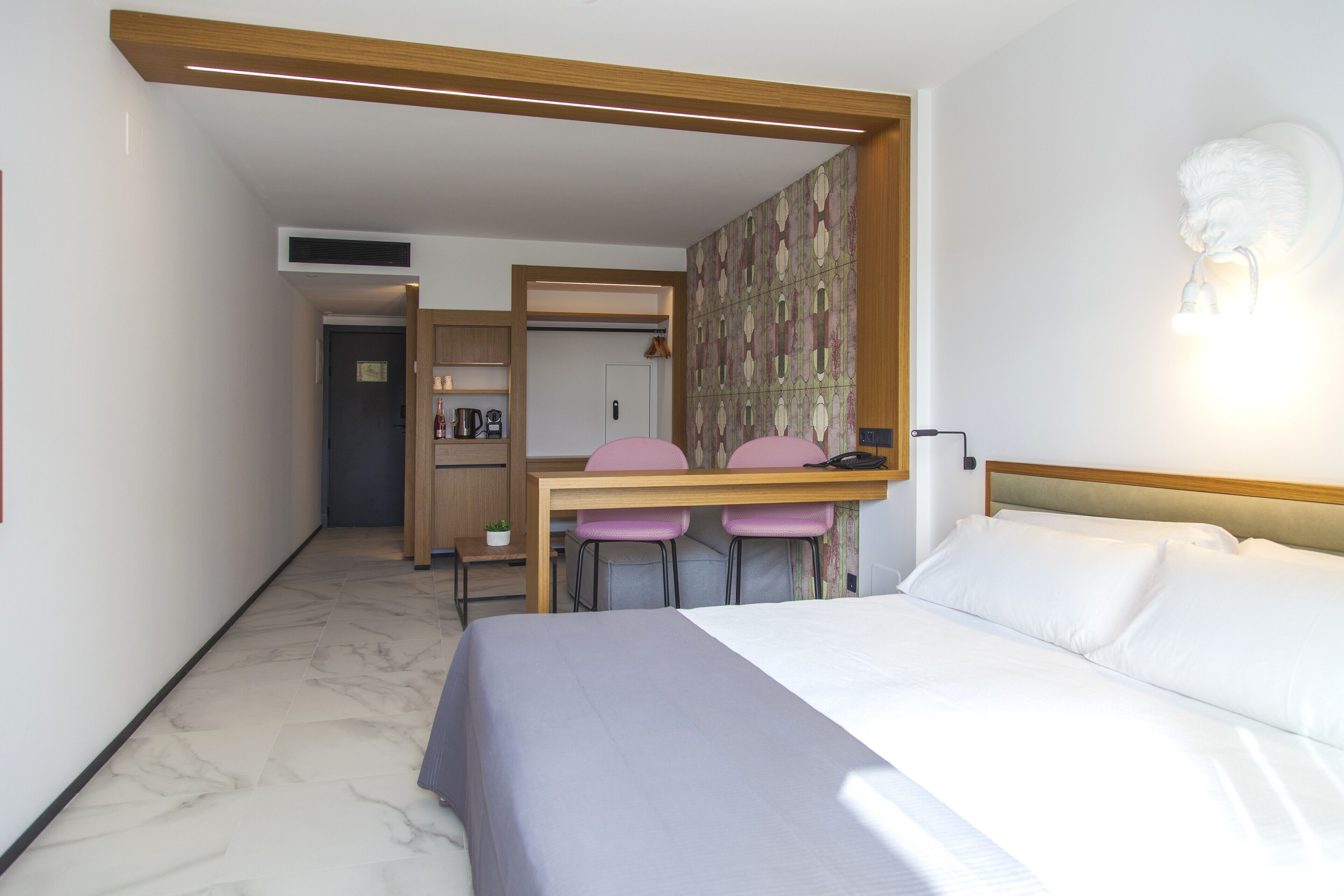 Une chambre d’hôtel comprenant un lit, un bureau avec deux chaises, une petite kitchenette et un élément décoratif mural.