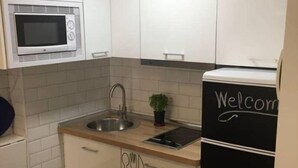 A compact kitchen with white cabinets, a microwave, a sink, and a refrigerator with a "Welcome" sign. - Downtown beach & peace (Málaga)
