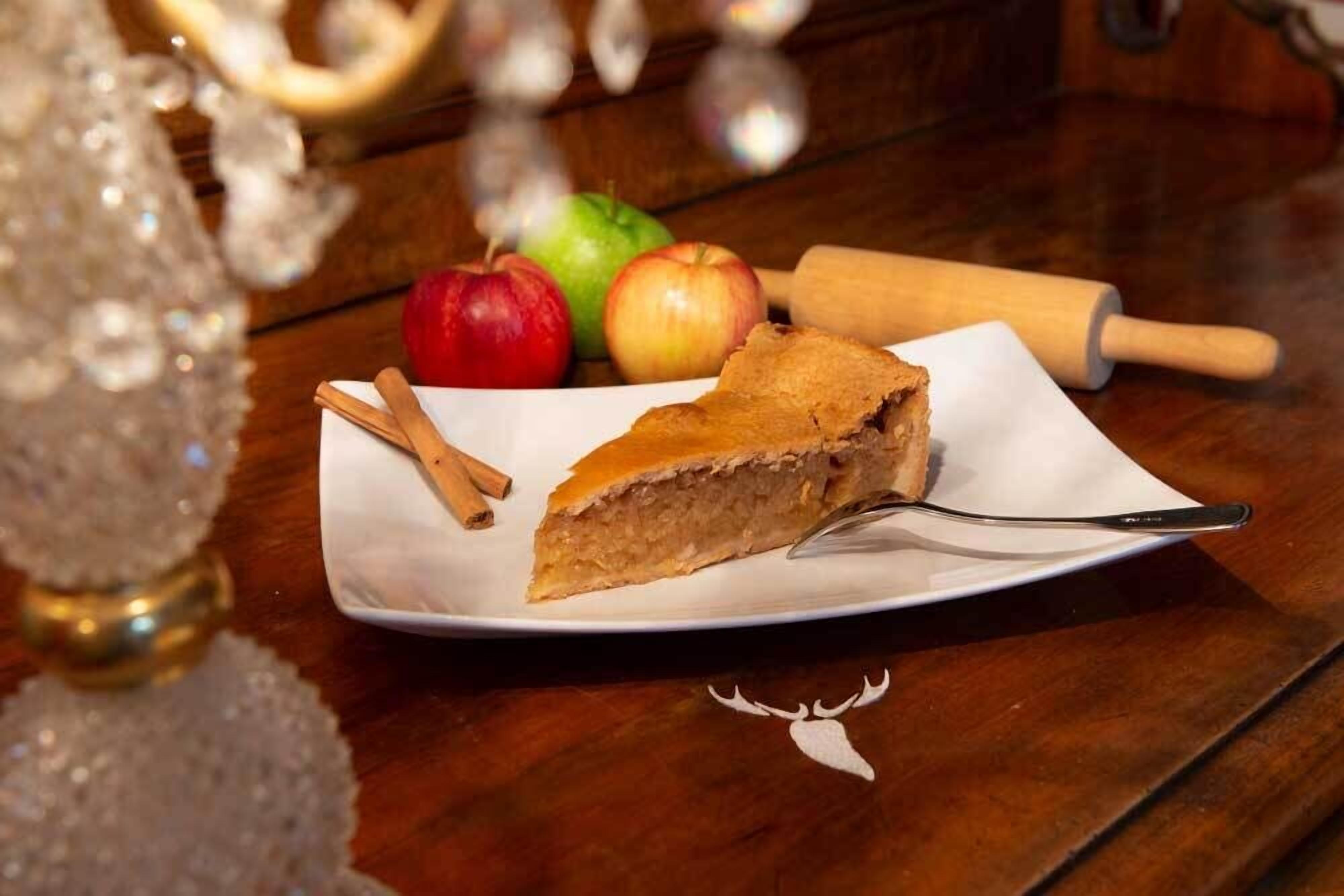 Ein Stück Kuchen auf einem weißen Teller mit Zimstangen daneben, auf einem Holztisch platziert.