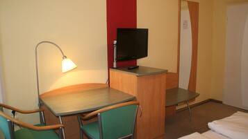 A hotel room with a desk, two chairs, a television, a lamp, and a bed.