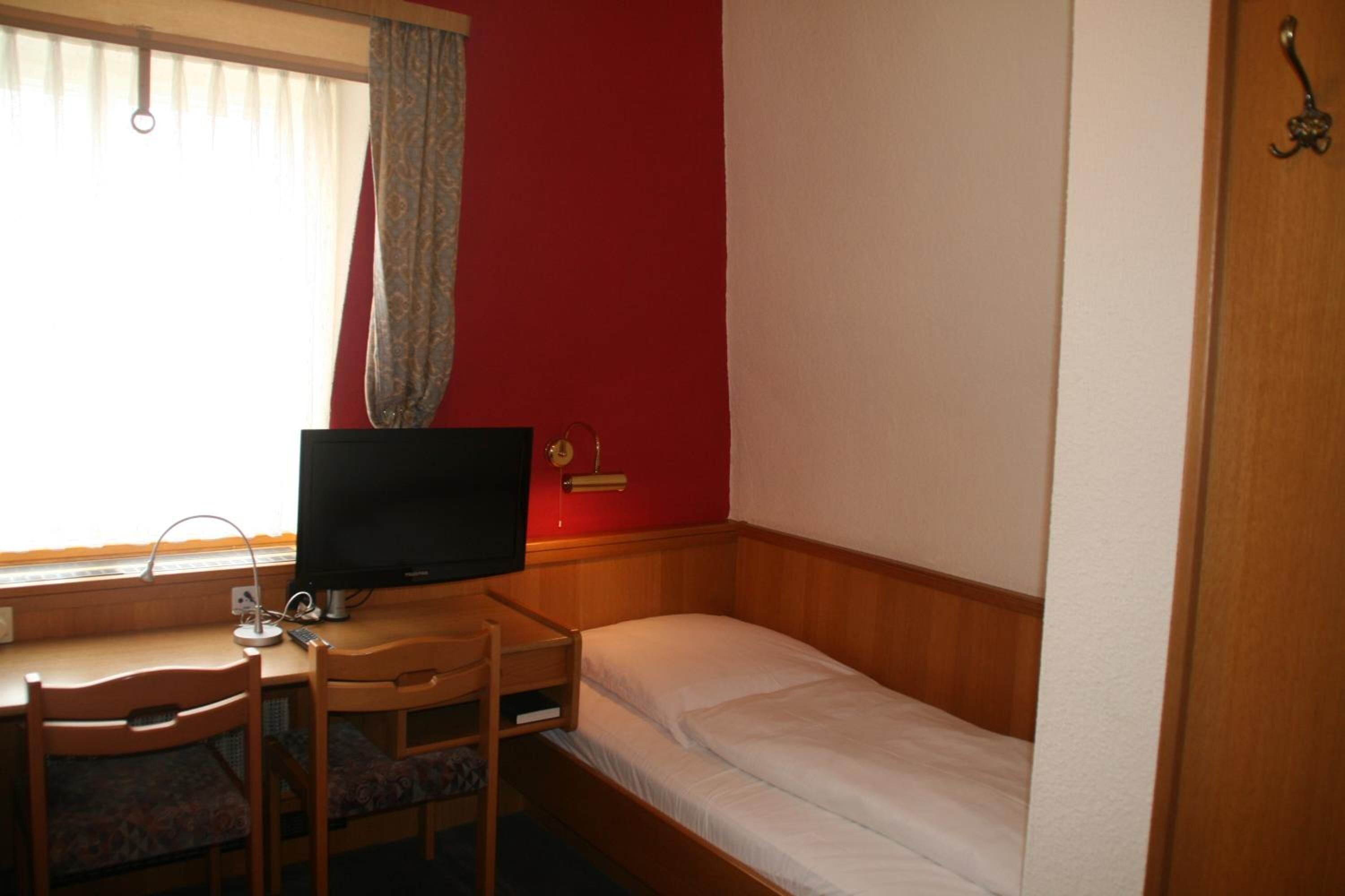 A small room with a single bed, a desk with a computer, and a chair.