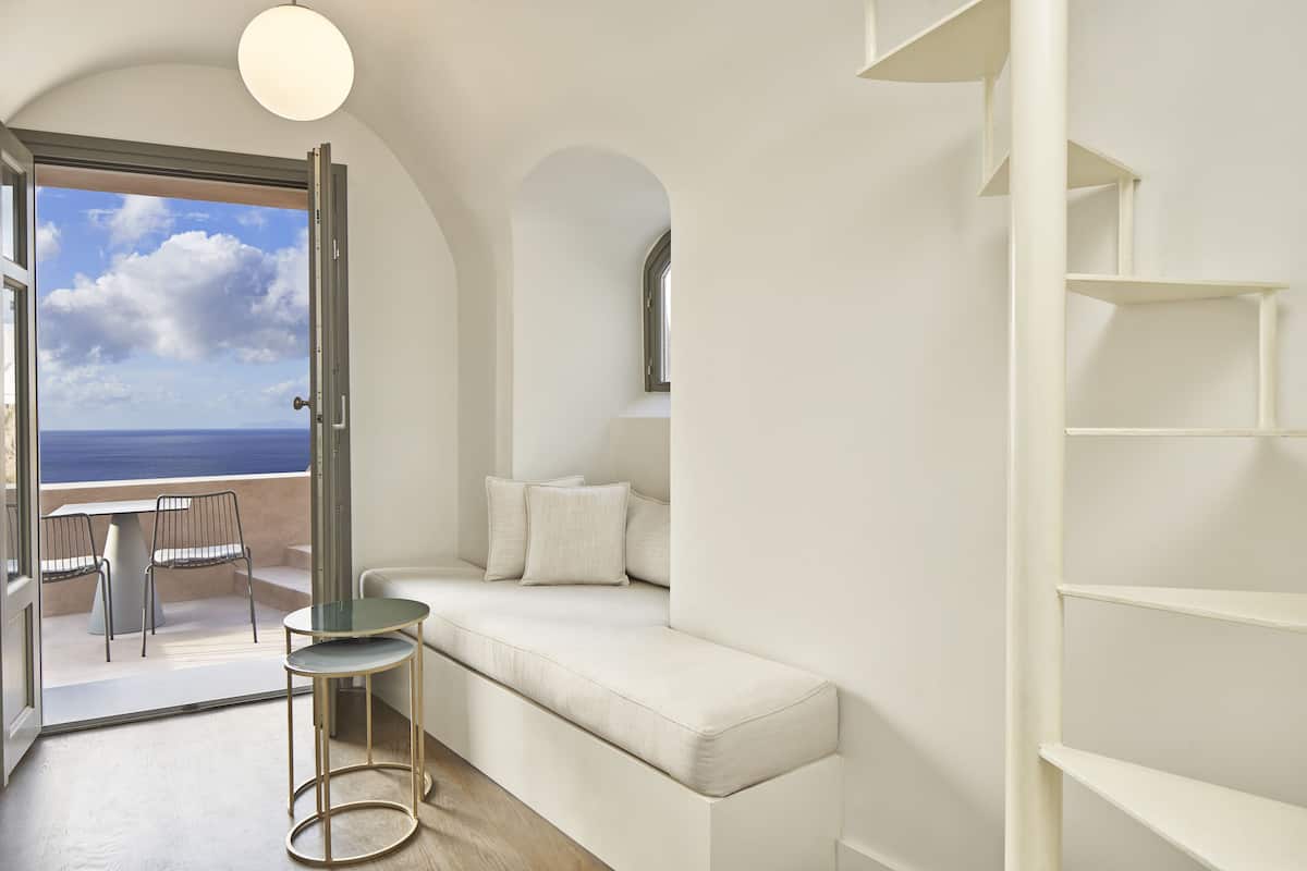 A modern interior with a white sofa, a small table, and a view of the ocean through an open door.