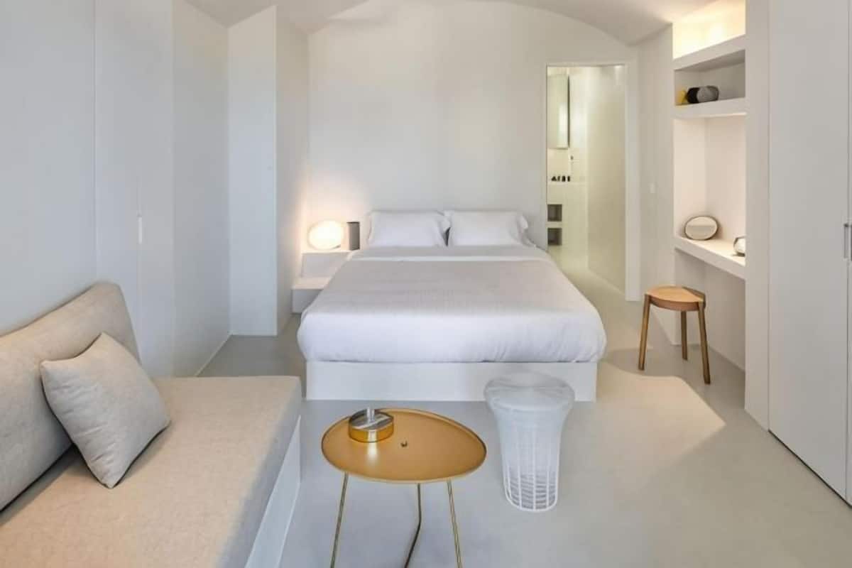 A modern bedroom with a bed, bedside tables, a small stool, and a chair.