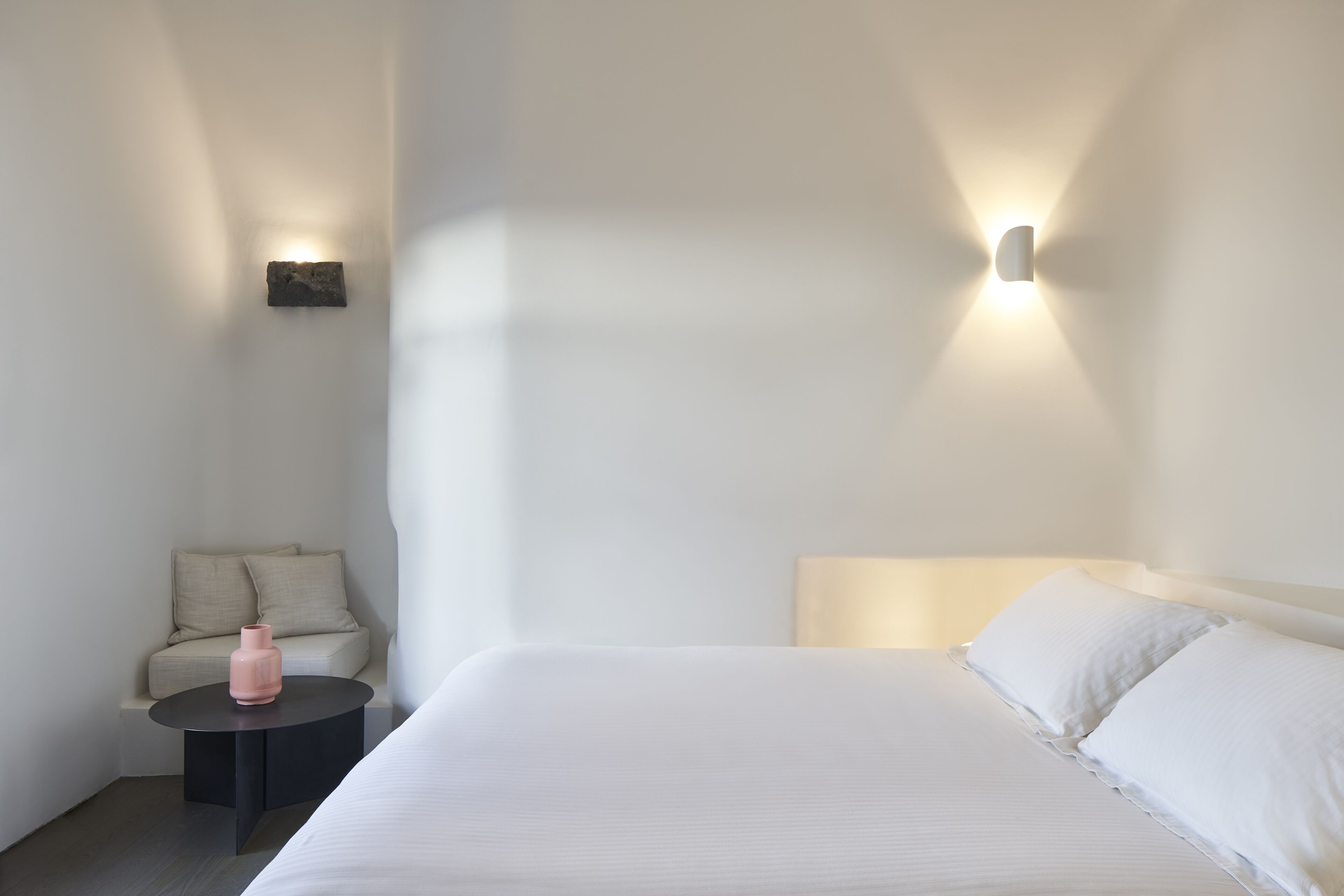 Una habitación de hotel minimalista con una cama grande, una pequeña mesa redonda y un sofá.