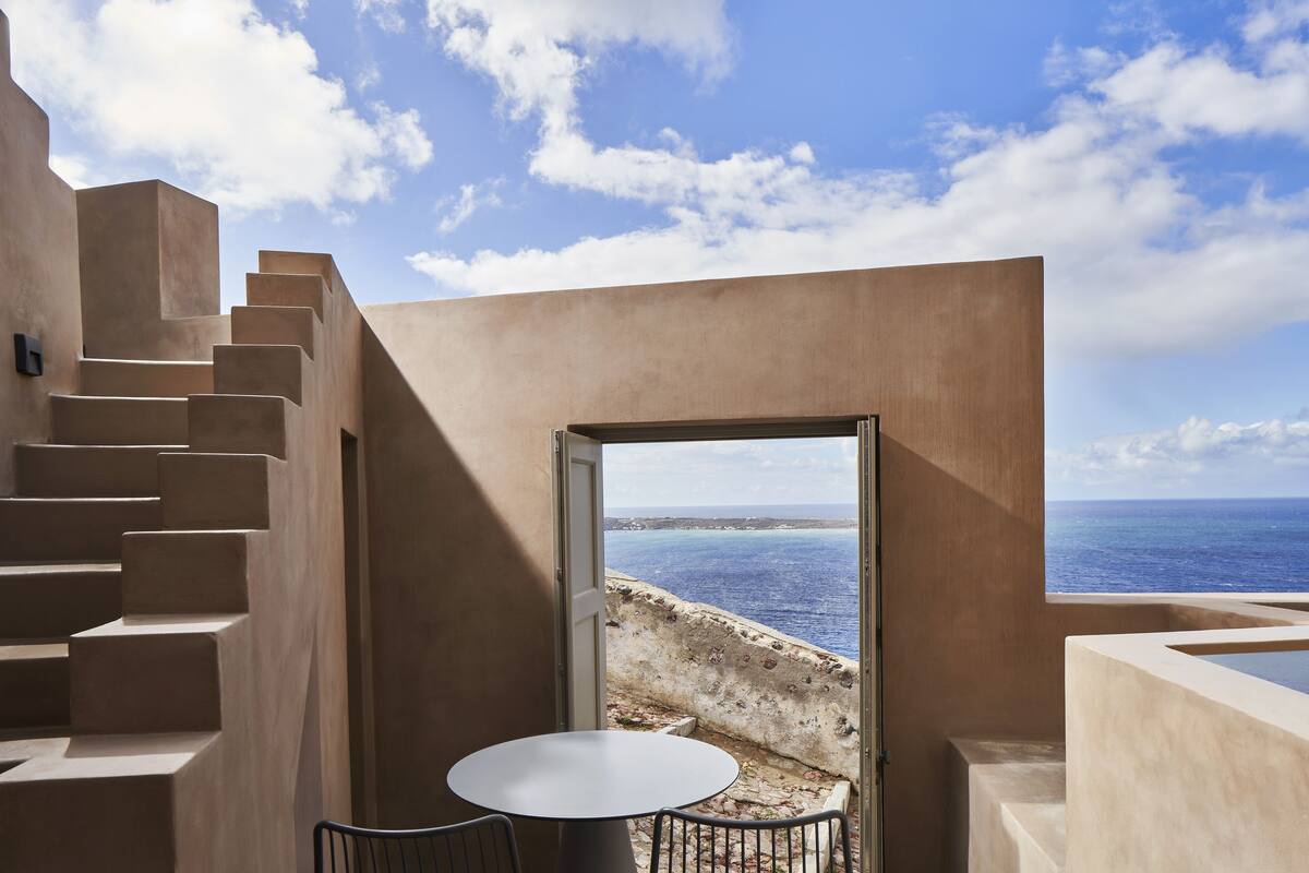 A modern interior with a staircase, a table, and a view of the sea.