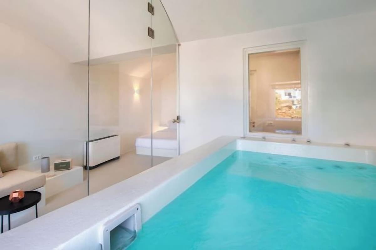 Une piscine intérieure moderne avec un mur en verre, un canapé blanc et une petite table.