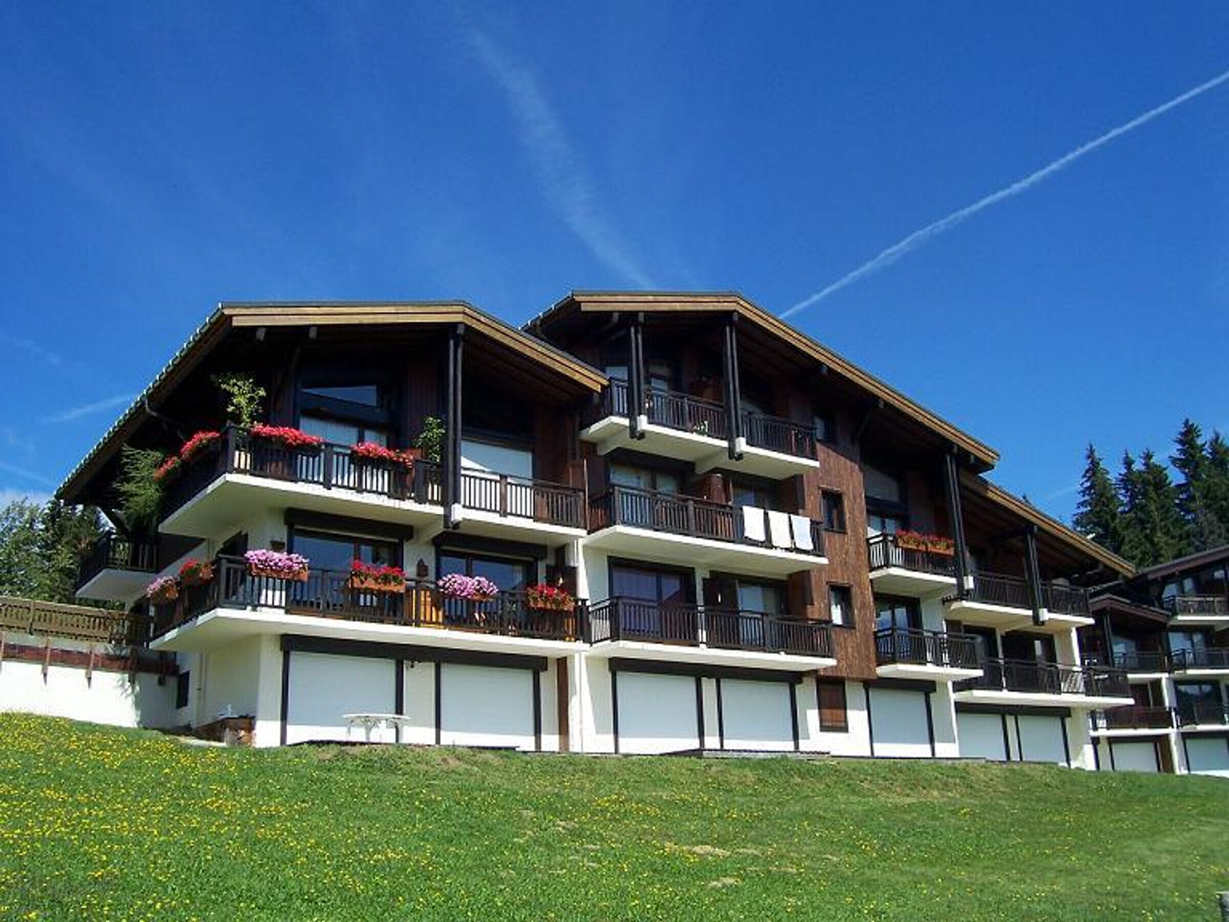 A multi-story hotel with balconies adorned with flowers, set against a clear blue sky.
