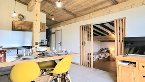 A compact kitchen with wooden cabinets, a dining table with yellow chairs, and a TV in a bedroom with a bunk bed. - Quiet apartment near slopes, 6 ppl, parking (Notre-Dame-de-Bellecombe)