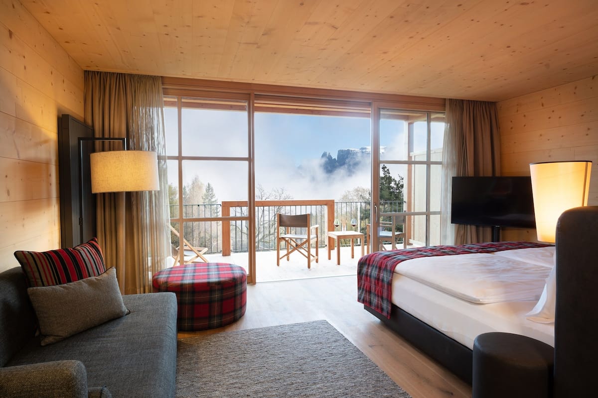 Une chambre d’hôtel moderne dotée d’un grand lit, d’un canapé, d’une télévision et d’un balcon offrant une vue sur les montagnes.