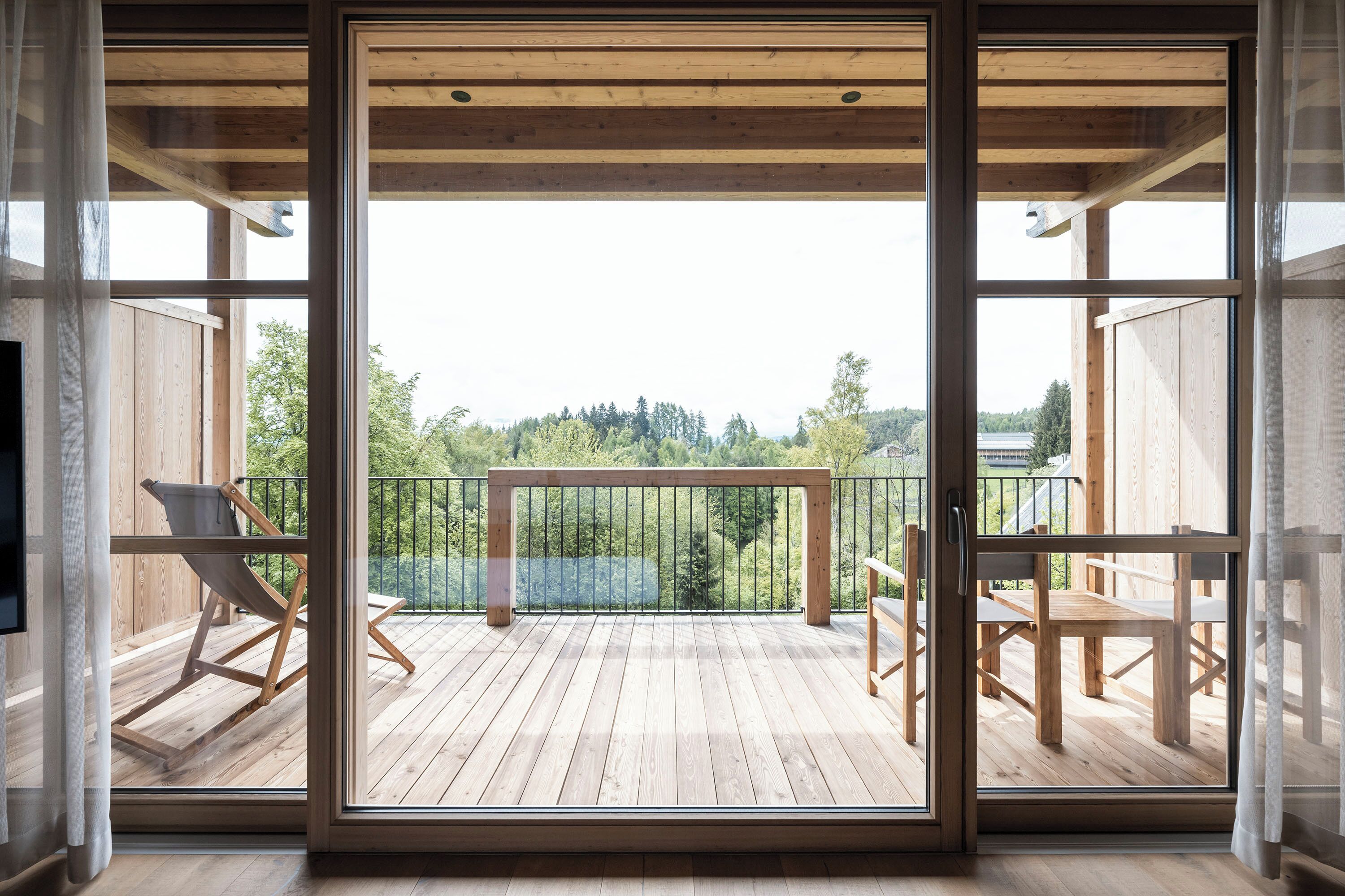 A wooden deck with a glass door leading to a balcony, furnished with chairs and a table.