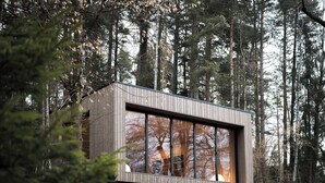Una cabaña moderna con ventanas amplias, rodeada de un bosque.