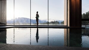 A person standing by a large indoor pool with a view of mountains through large windows.