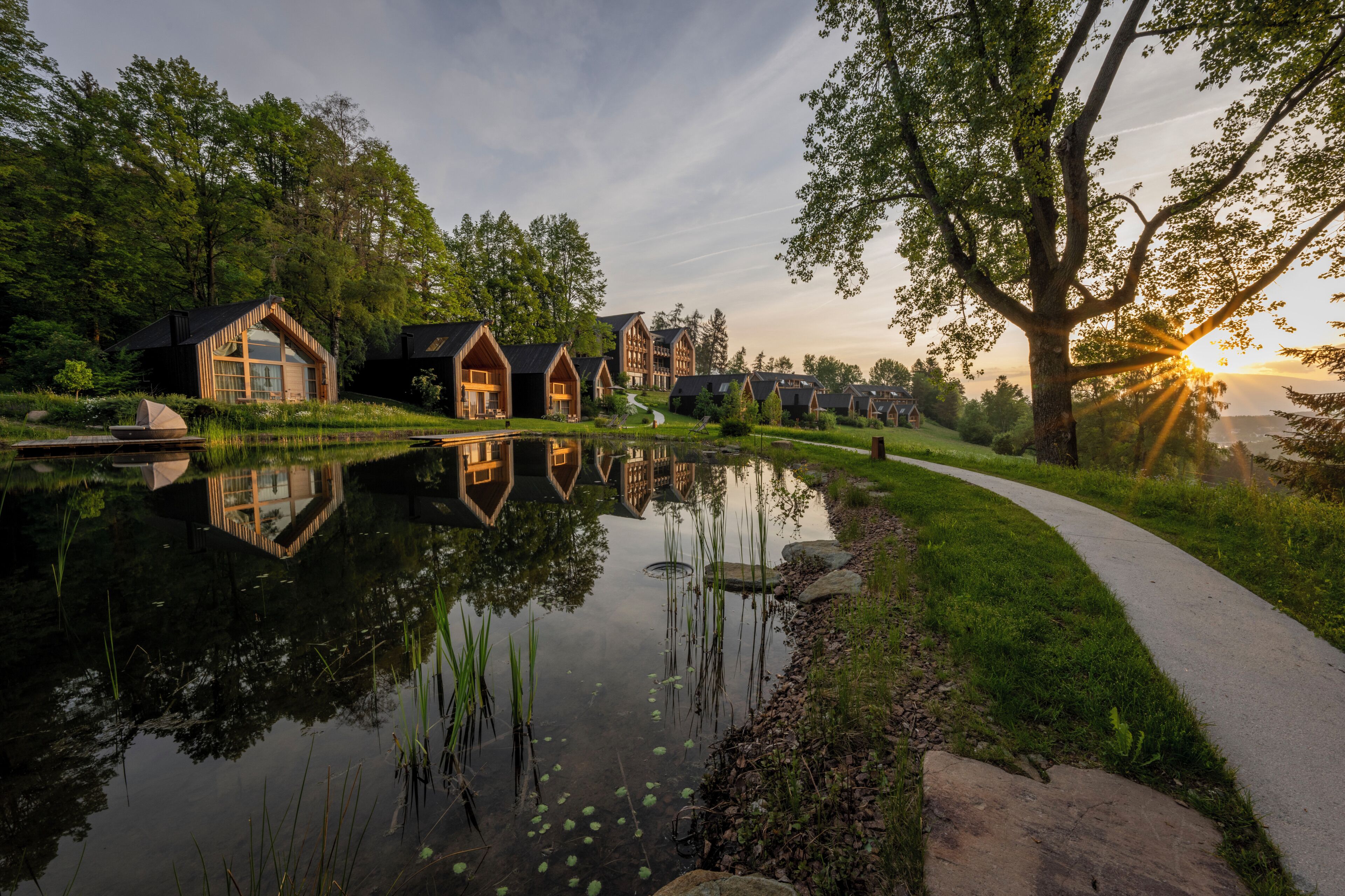 A row of wooden cabins with a pond in the foreground and a walking path.