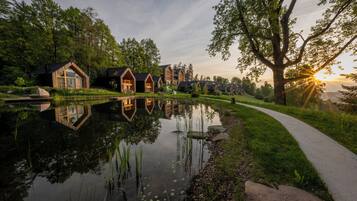 A row of wooden cabins with a pond in the foreground and a walking path.
