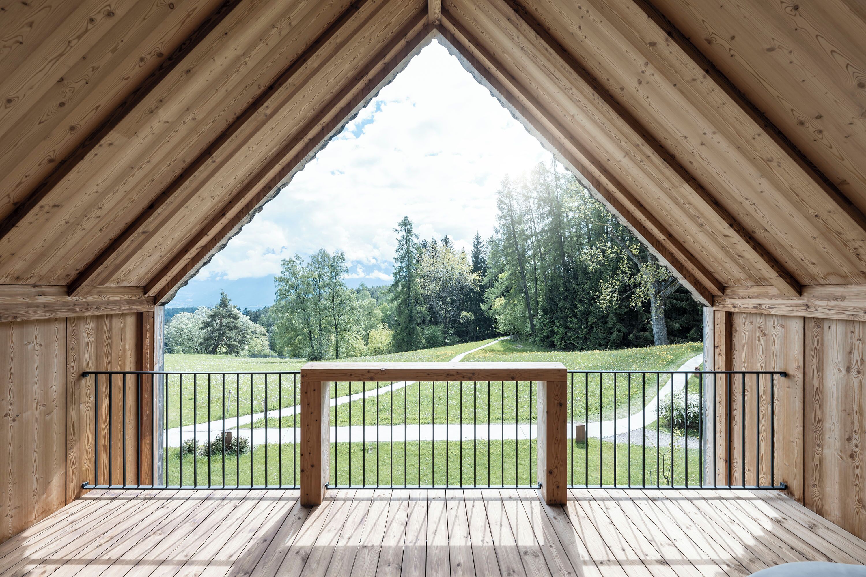 Een houten terras met een metalen hekwerk, met uitzicht op een groen landschap met bomen en een pad.