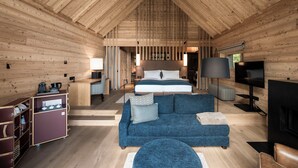 A log cabin interior with a large bed, a sofa, a TV, and a kitchenette.