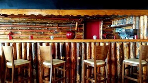 Un coin bar rustique avec des murs en bois et un comptoir en bois. On y trouve quatre tabourets de bar en bois et une pomme rouge posée sur le comptoir.