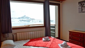 Une chambre d’hôtel avec un lit, une commode en bois, une fenêtre donnant sur un paysage enneigé et un radiateur.