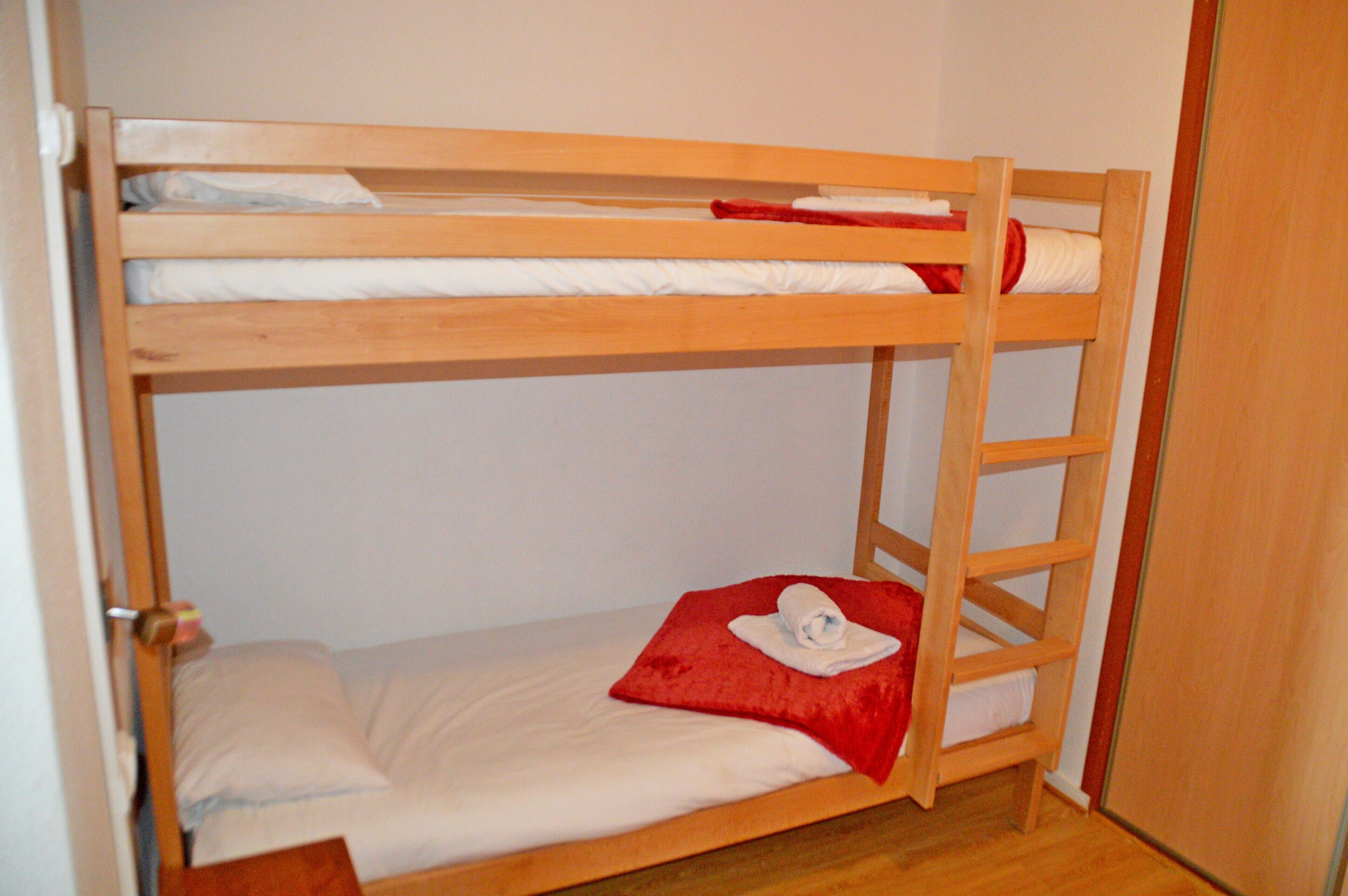 A bunk bed with a ladder, a red pillow, and a white blanket.