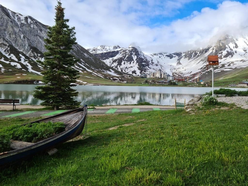 A lakeside view with mountains, a wooden boat, and a bench.