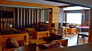 Une pièce confortable, aménagée dans le style d’un chalet, avec des meubles en bois, une table de billard et une grande fenêtre laissant entrer la lumière naturelle.