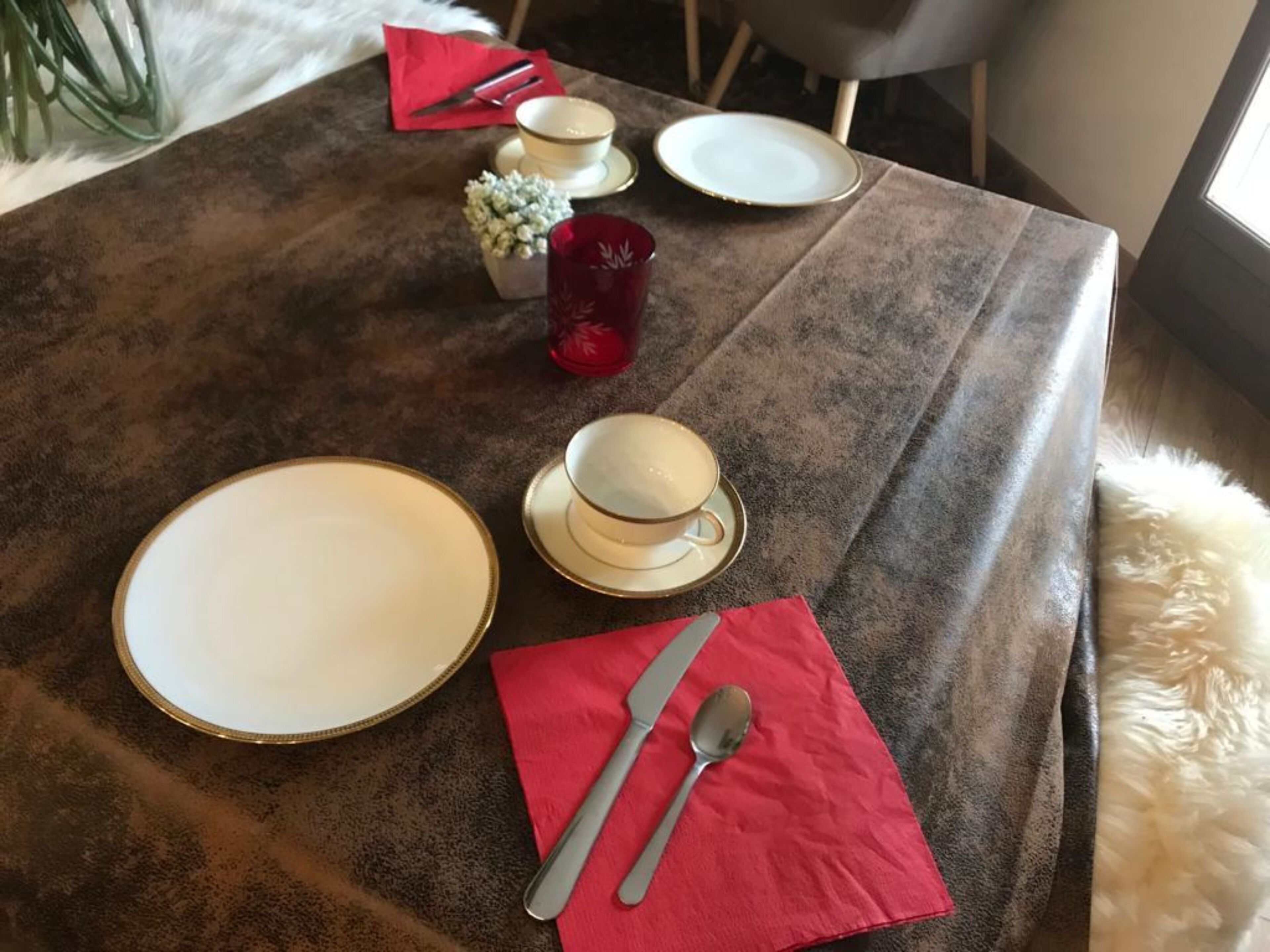 A dining table set with plates, a cup, a spoon, and a red napkin.