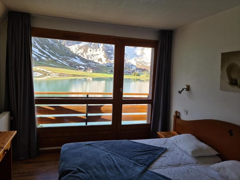 A room with a bed, a view of a lake, and mountains in the background.