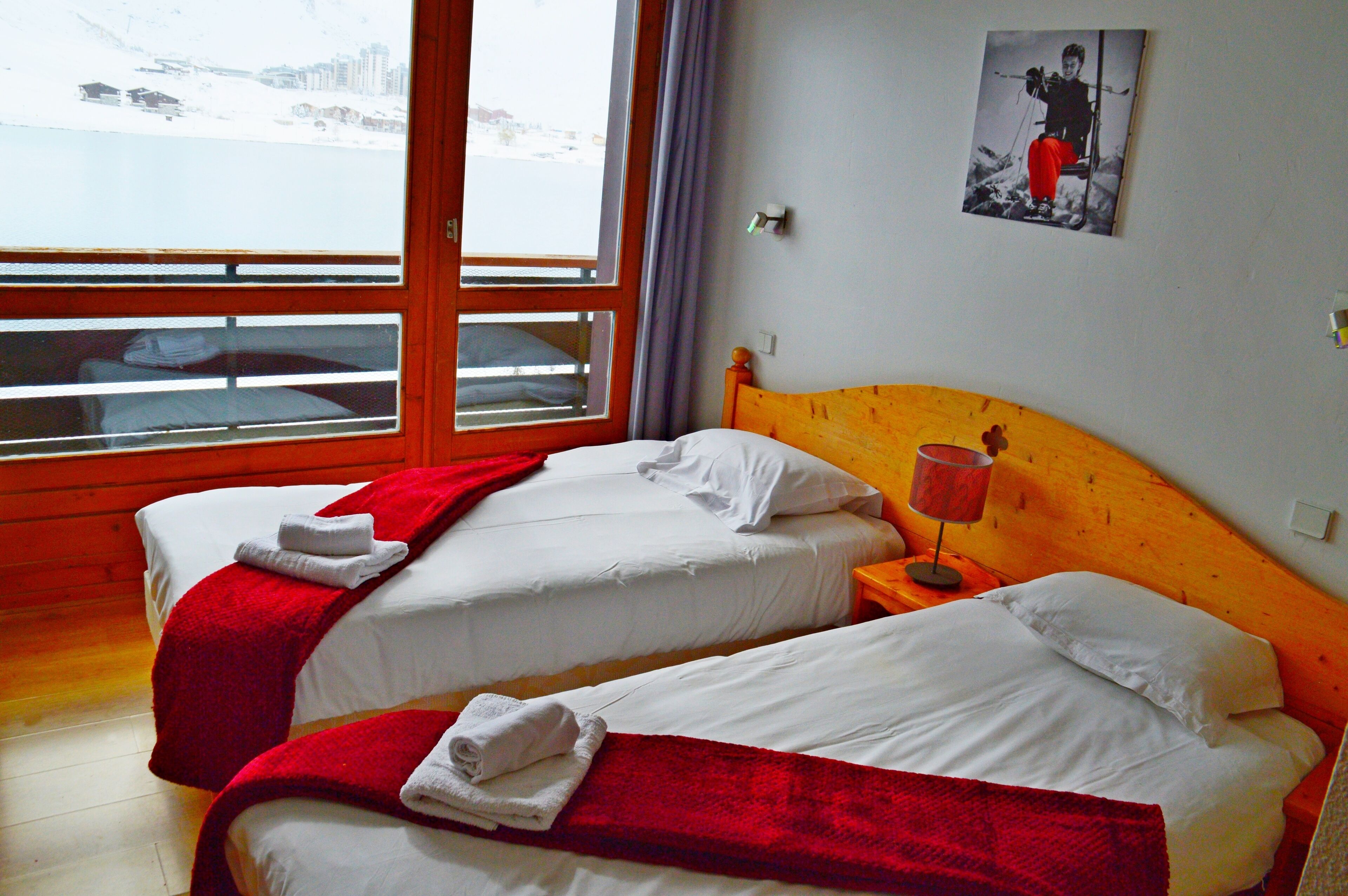 Quarto de hotel com duas camas, janela com vista para uma paisagem nevada e cabeceira de madeira.