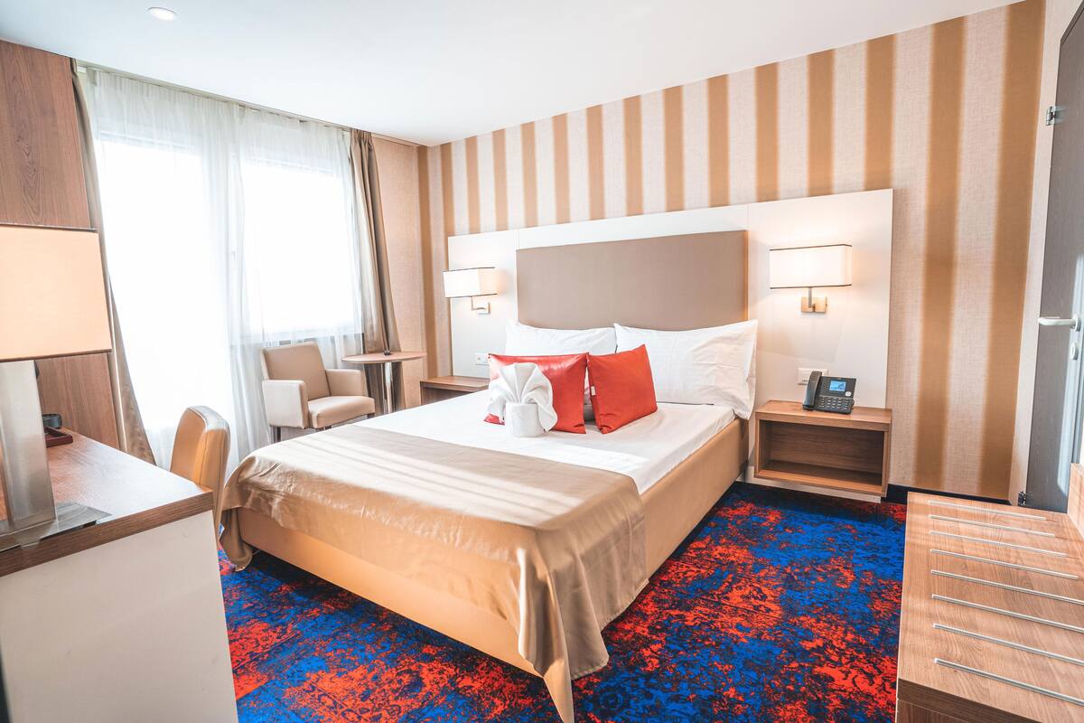 A hotel room with a large bed, bedside tables, a desk, and a chair.