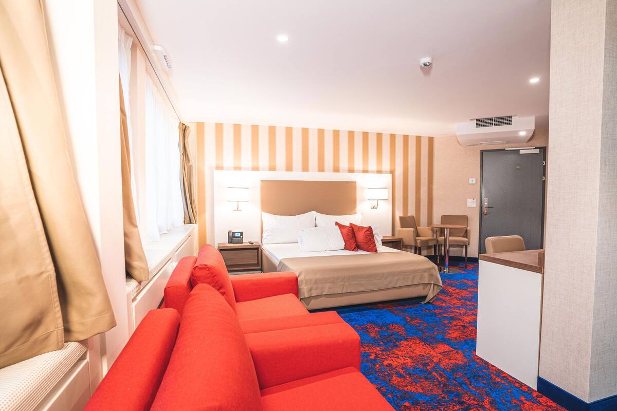 A hotel room with a bed, a desk, a sofa, and a carpeted floor.