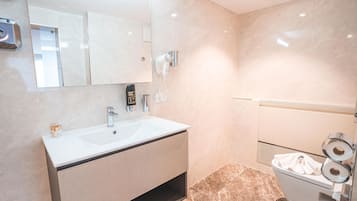 Ein modernes Badezimmer mit einem großen Spiegel, einem Waschbecken, einem Föhn und einer Toilette mit Toilettenpapier.