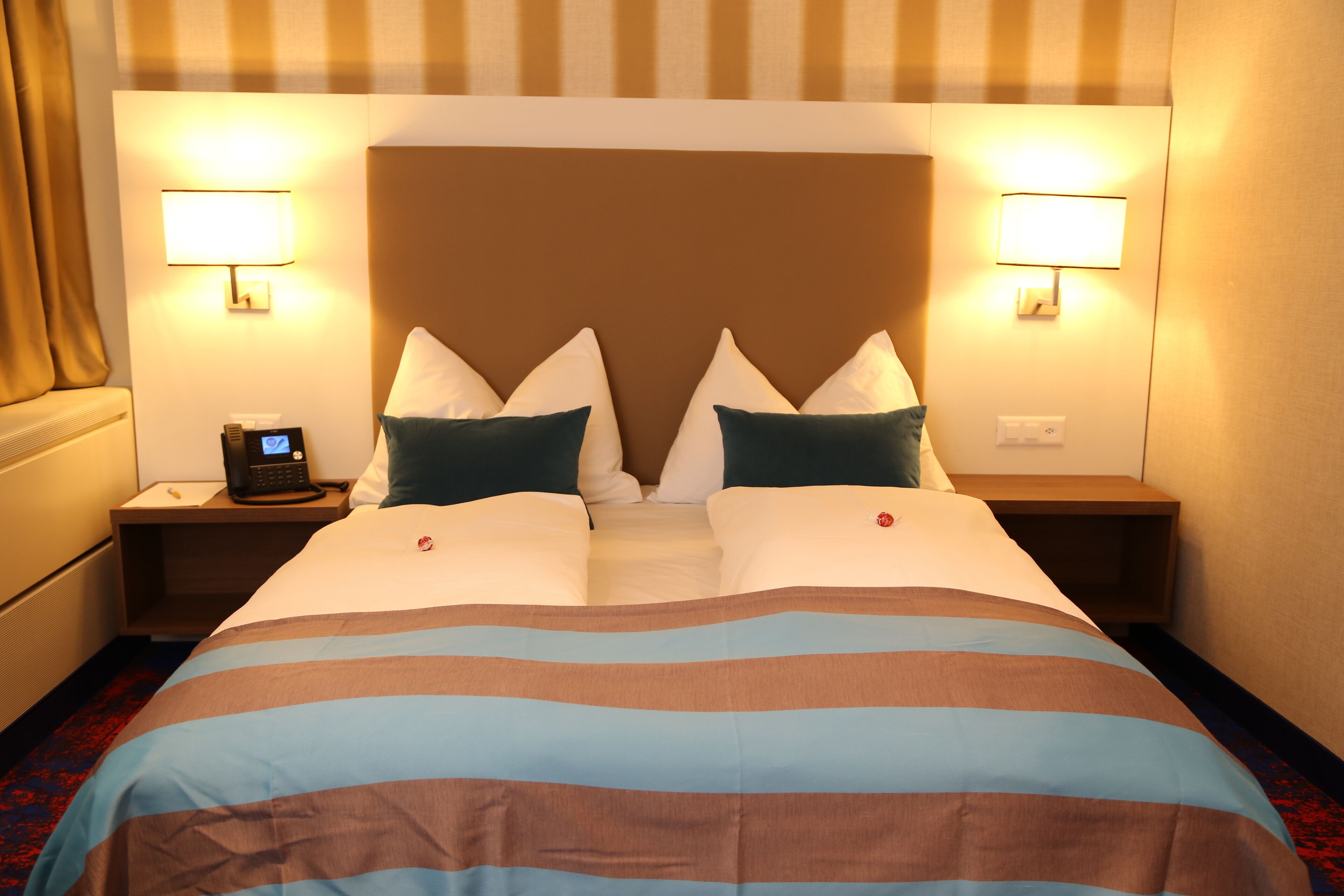 Habitación de hotel con una cama grande, dos lámparas de noche, una mesita de noche con teléfono y alfombra roja.