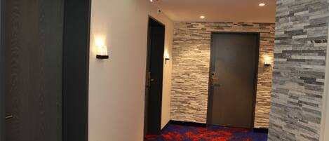 A hallway with a red carpet, a stone wall, and a door with a light switch.