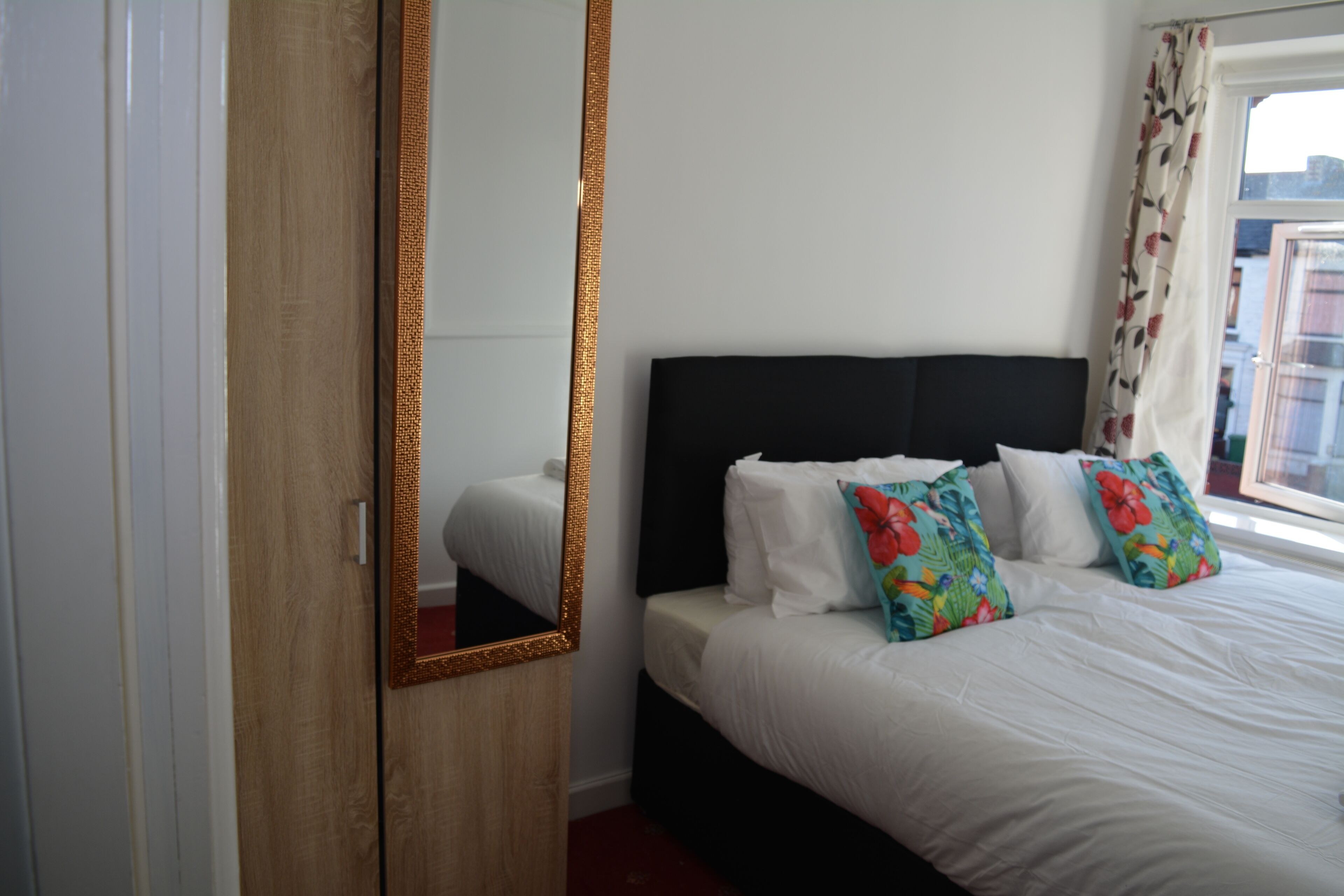 A bedroom with a large mirror, a black headboard, white bedding, and colorful pillows.