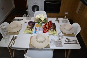 A dining table set with white plates, bowls, cutlery, and a vase of white flowers. - Luxury Apartment - Central Cardiff (Cardiff)