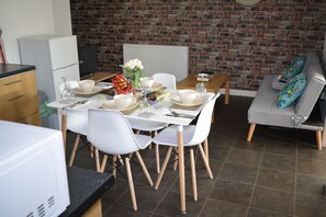 A dining area with a brick wall, white chairs, and a grey sofa. - Luxury Apartment - Central Cardiff (Cardiff)