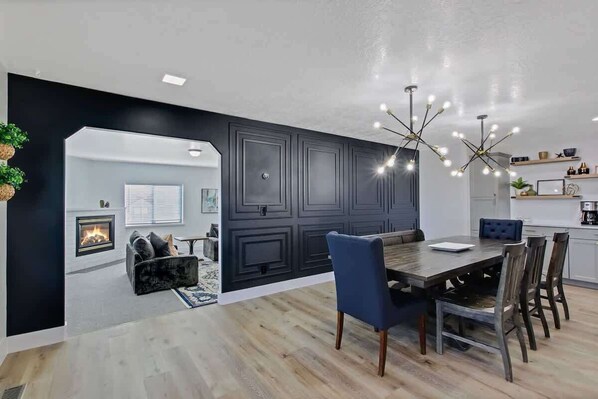 A modern kitchen with dark cabinetry, a dining area with a wooden table and chairs, and a fireplace.