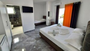 A modern hotel room with a large bed, a separate sitting area, a flat-screen TV, and a bathroom with a shower and toilet. - Hotel Seadel (Ksamil)