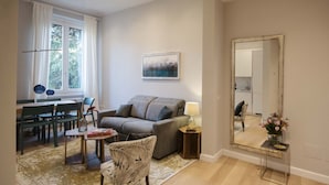A living room with a sofa, a chair, a dining table, and a large mirror. - Apartments Florence- Oblate Exclusive View	 (Firenze)