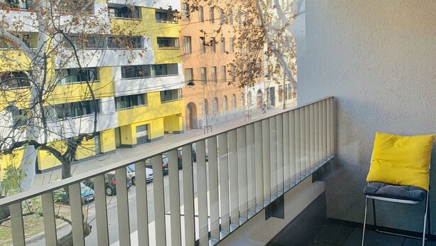 A balcony with a metal railing, a yellow cushion, and a chair. - Central luxury apartment close to Prater / Messe / WU (Leopoldstadt)