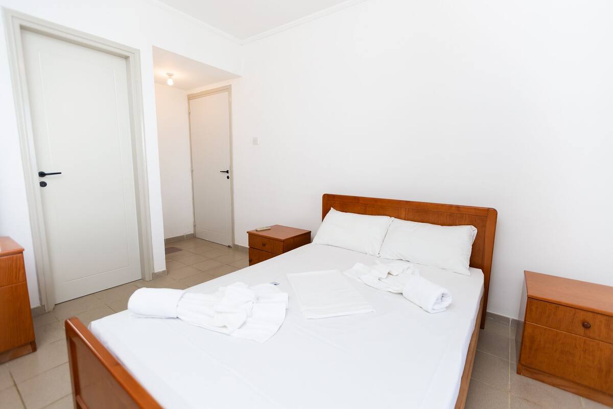 A clean, well-lit hotel room with a large bed, wooden headboard, two bedside tables, and a wardrobe.